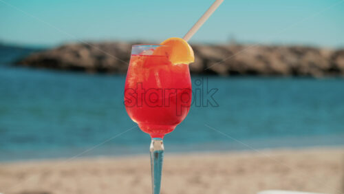 Video - Refreshing red orange cocktail with ice and orange slice against the deep blue Mediterranean Sea