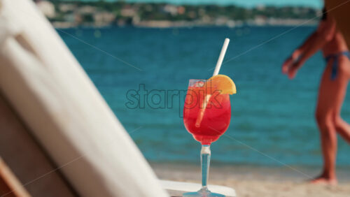 Video - Refreshing red orange cocktail with ice and orange slice against the deep blue Mediterranean Sea