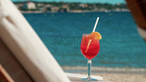 Video - Refreshing red orange cocktail with ice and orange slice against the deep blue Mediterranean Sea