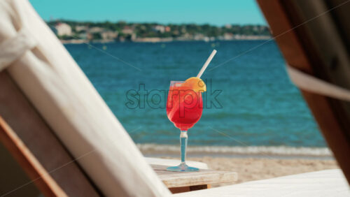 Video - Refreshing red orange cocktail with ice and orange slice against the deep blue Mediterranean Sea