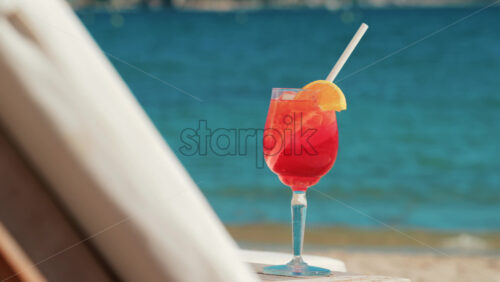 Video - Refreshing red orange cocktail with ice and orange slice against the deep blue Mediterranean Sea