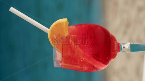 Video - Close up of a refreshing red orange cocktail with orange slice and ice cubes, captured outdoors on a sunny day in Cannes. Vertical