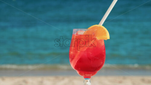 Video - Refreshing red orange cocktail with ice and orange slice against the deep blue Mediterranean Sea