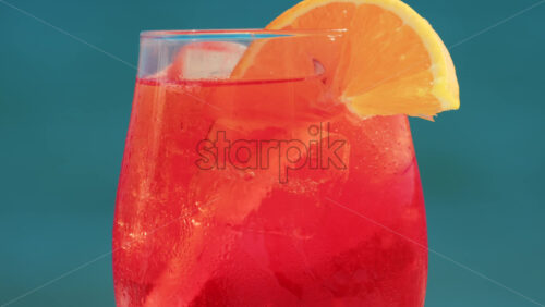 Video - Close up of a refreshing red orange cocktail with orange slice and ice cubes, captured outdoors on a sunny day in Cannes