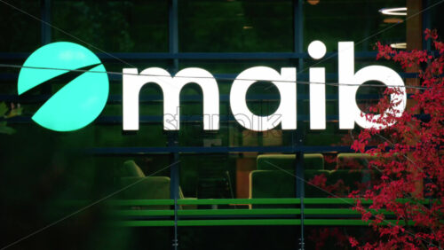 Video - Chisinau, Moldova - October 1, 2025: Modern glass building facade with the illuminated maib logo and red autumn leaves in the foreground