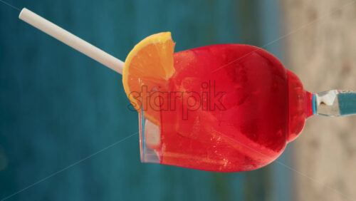 Video - Close up of a refreshing red orange cocktail with orange slice and ice cubes, captured outdoors on a sunny day in Cannes. Vertical