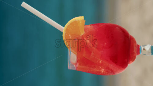 Video - Close up of a refreshing red orange cocktail with orange slice and ice cubes, captured outdoors on a sunny day in Cannes. Vertical