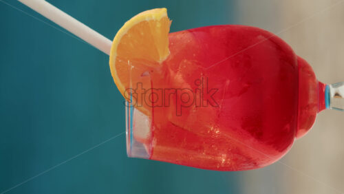 Video - Close up of a refreshing red orange cocktail with orange slice and ice cubes, captured outdoors on a sunny day in Cannes. Vertical