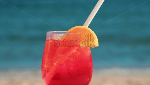 Video - Close up of a refreshing red orange cocktail with orange slice and ice cubes, captured outdoors on a sunny day in Cannes