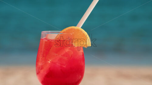 Video - Refreshing red orange cocktail with ice and orange slice against the deep blue Mediterranean Sea