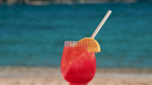 Video - Refreshing red orange cocktail with ice and orange slice against the deep blue Mediterranean Sea