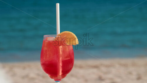 Video - Refreshing red orange cocktail with ice and orange slice against the deep blue Mediterranean Sea