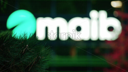 Video - Chisinau, Moldova - October 1, 2025: Modern glass building facade with the illuminated maib logo and red autumn leaves in the foreground