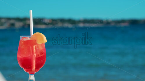 Video - Refreshing red orange cocktail with ice and orange slice against the deep blue Mediterranean Sea