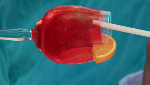Video - Close up of a refreshing red orange cocktail with orange slice and ice cubes, captured outdoors on a sunny day in Cannes. Vertical