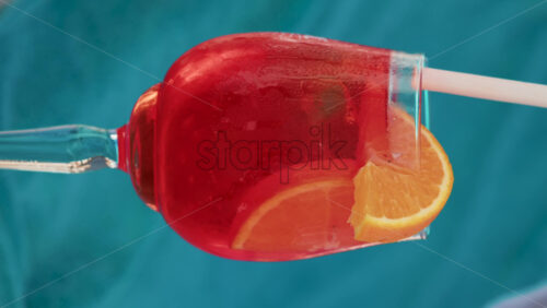 Video - Close up of a refreshing red orange cocktail with orange slice and ice cubes, captured outdoors on a sunny day in Cannes. Vertical