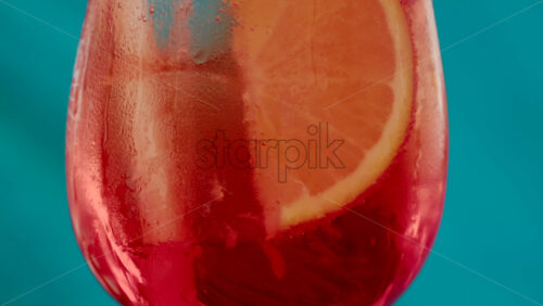 Video - Close up of an orange slice and ice cubes in a glass of red orange with condensation
