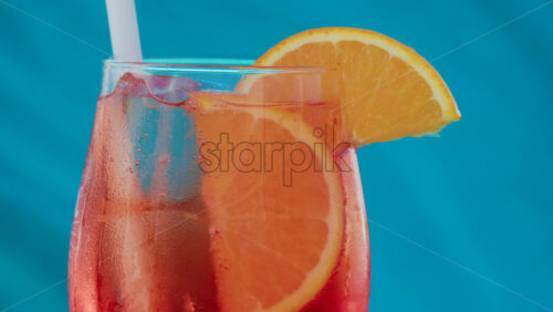 Video - Close up of an orange slice and ice cubes in a glass of red orange with condensation
