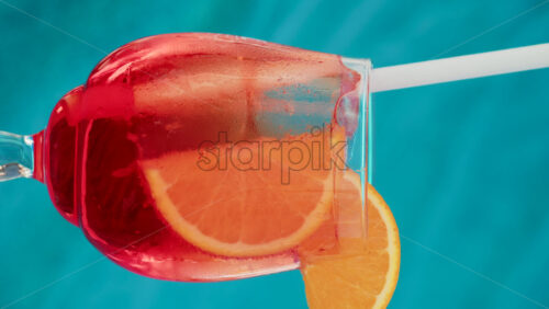 Video - Close up of an orange slice and ice cubes in a glass of red orange with condensation. Vertical
