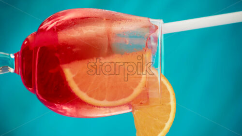 Video - Close up of an orange slice and ice cubes in a glass of red orange with condensation. Vertical