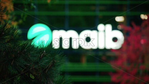 Video - Chisinau, Moldova - October 1, 2025: Modern glass building facade with the illuminated maib logo and red autumn leaves in the foreground