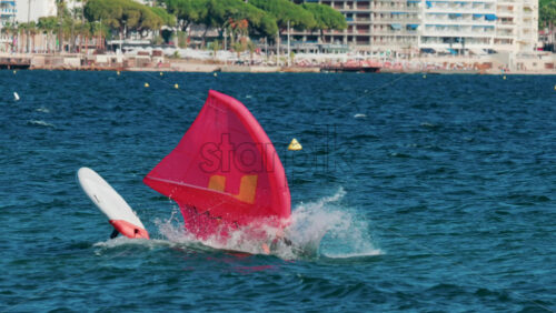 Video - A man in a wetsuit falling down while wing foiling with a bright pink sail on the blue Mediterranean waters of Cannes, France