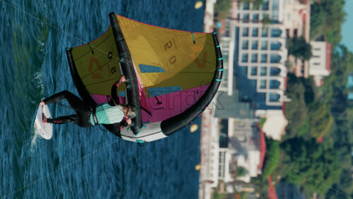 Video - Cannes, France - October 6, 2025: A woman balances on a wing foil board holding a colorful yellow and pink sail on a sunny day. Vertical
