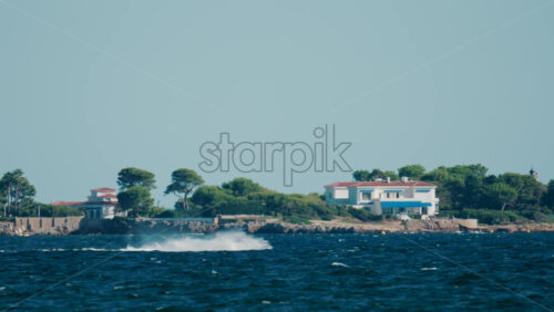 Video - Man riding a jet ski across the sparkling blue waters near Cannes, France, with green hills and villas in the background