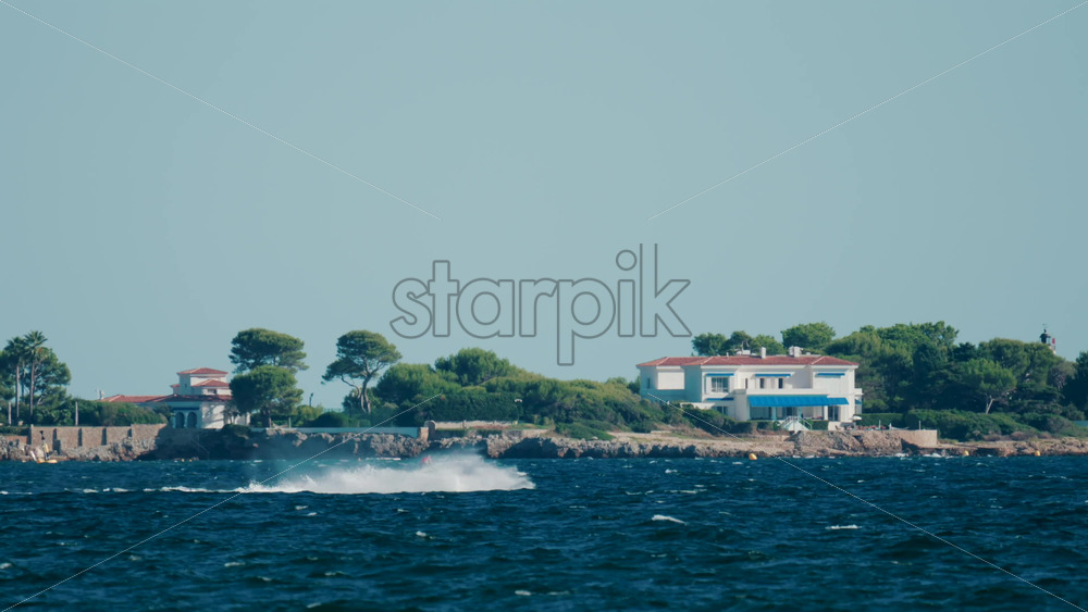 Video - Man riding a jet ski across the sparkling blue waters near Cannes, France, with green hills and villas in the background