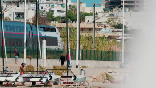 Video - Cannes, France - October 6, 2025: A modern train passes along the coastline near the beach, while people walk and relax nearby
