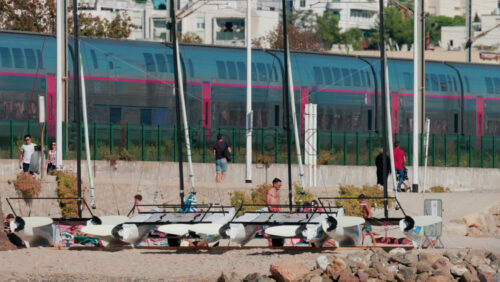 Video - Cannes, France - October 6, 2025: A modern train passes along the coastline near the beach, while people walk and relax nearby