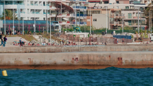 Video - Cannes, France - October 6, 2025: A modern train passes along the coastline near the beach, while people walk and relax nearby