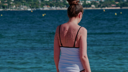 Video - A young woman walks slowly into the calm turquoise water on a sunny summer day in Cannes, France