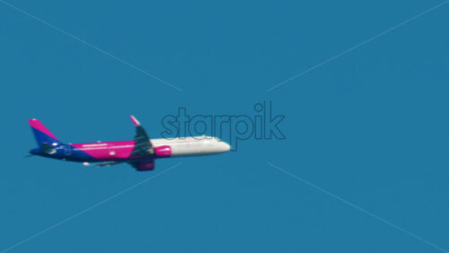Video - Cannes, France - October 6, 2025: A pink and blue passenger airplane flies high above the city against a bright blue sky