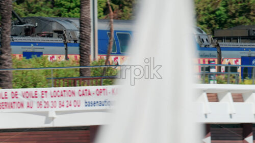 Video - Cannes, France - October 7, 2025: A blue regional train passes near palm trees and a street