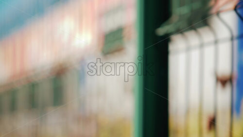 Video - A modern train seen through a green metal fence with a shallow depth of field