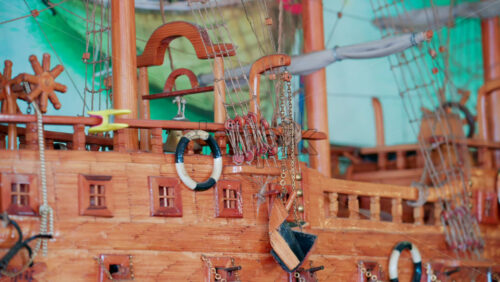 Video - Close up of a beautifully crafted wooden ship model with intricate rigging and lifebuoys, displayed against a colorful nautical background