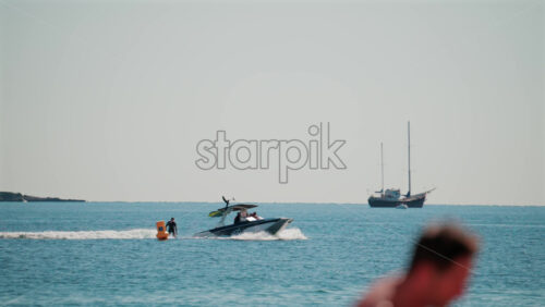 Video - Cannes, France - October 7, 2025: A fast motorboat pulls an inflatable raft across the calm blue sea, while distant yachts rest on the horizon