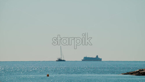 Video - A cruise ship and a sailing boat move slowly on a shimmering blue sea under clear sunlight