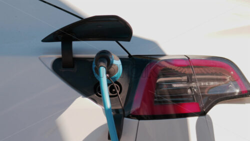 Video - Close up of an electric car plugged into a blue charging cable in daylight