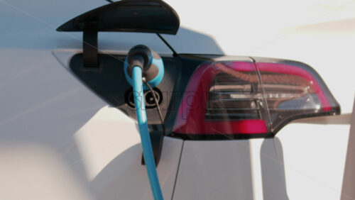 Video - Close up of an electric car plugged into a blue charging cable in daylight