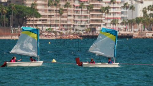 Video - Cannes, France - October 7, 2025: Children in small sailboats learning to navigate on the blue sea near a beach resort