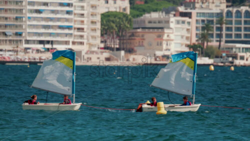 Video - Cannes, France - October 7, 2025: Children in small sailboats learning to navigate on the blue sea near a beach resort