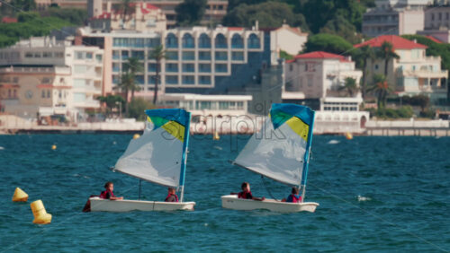 Video - Cannes, France - October 7, 2025: Children in small sailboats learning to navigate on the blue sea near a beach resort