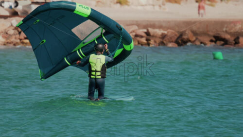 Video - Cannes, France - October 7, 2025: A man practices wing foiling, balancing on a board while holding an inflatable sail on turquoise water near the shore