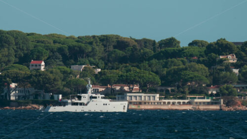 Video - A large white vessel sails along a scenic coastline surrounded by green trees and villas