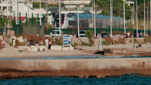 Video - Cannes, France - October 8, 2025: A modern train passes along the coastline near the beach, while people walk and relax nearby