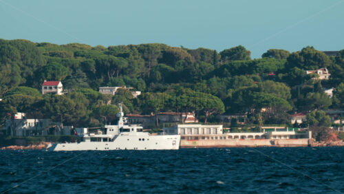 Video - Luxury white yacht sailing near Mediterranean coastline with elegant villas surrounded by trees