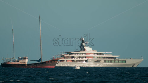 Video - Contrast between a large modern yacht and an old rustic ship floating on blue waves under clear skies
