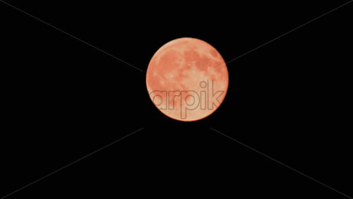 Video - A detailed close up of a full orange moon glowing brightly against a black night sky